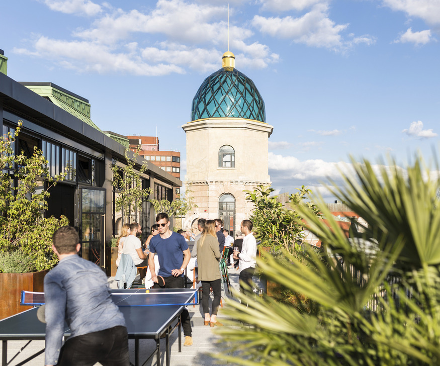 People play table tennis on a rooftop with a grand glass cupola behind the,