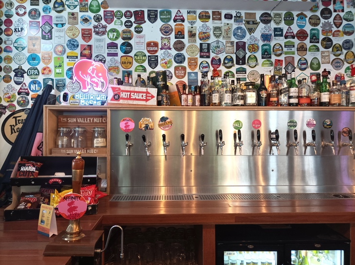 Brewery taprooms in London: An array of craft beer taps with aluminium backing - and scores of beer badges stuck on the wall behind