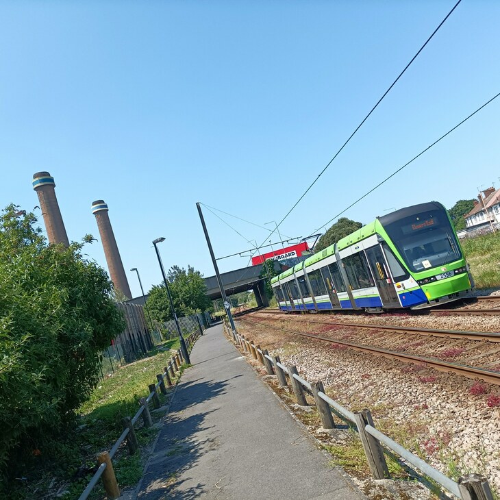 A green which and blue tram heading towards the camera, with two power station chimneys in the background