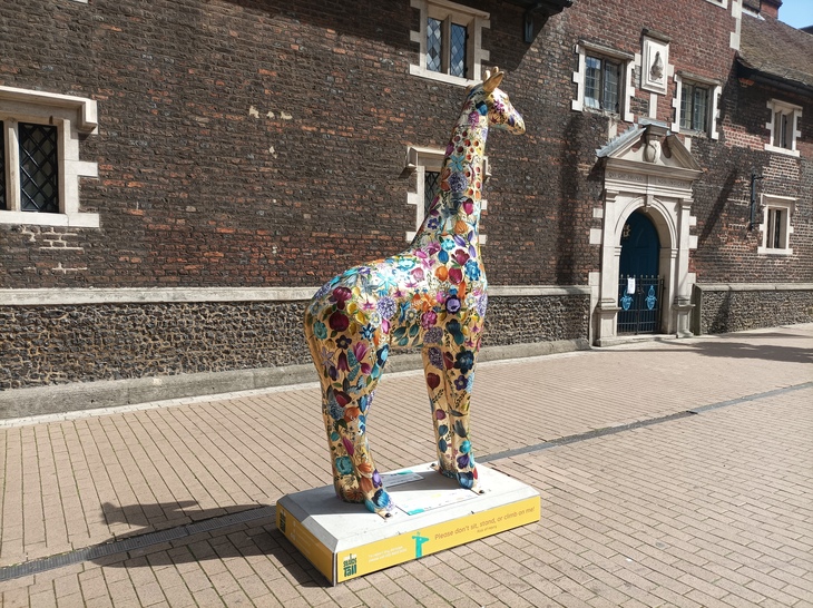 A golden giraffe sculpture in front of an Elizabethan building