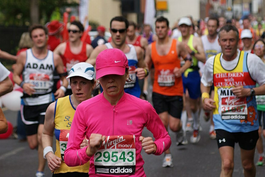 A woman in pink running top and hat running the London Marathon, with other runners also taking part behind her.