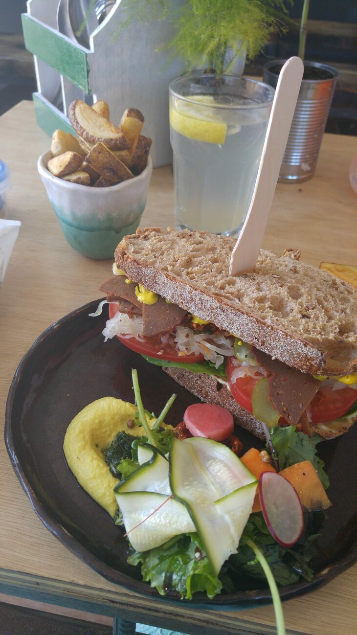 A vegan 'Reuben' sandwich and chips are on a wooden table. 