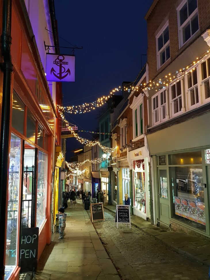 A steep traditional shopping street strung up with christmas lights at night time. 