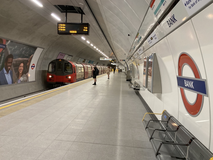 A tube train pulls up at a tube platform with a Bank roundel