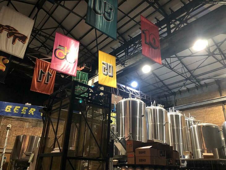 Brewery taprooms in London: Colourful flags flying from a huge warehouse with silver fermenting tanks