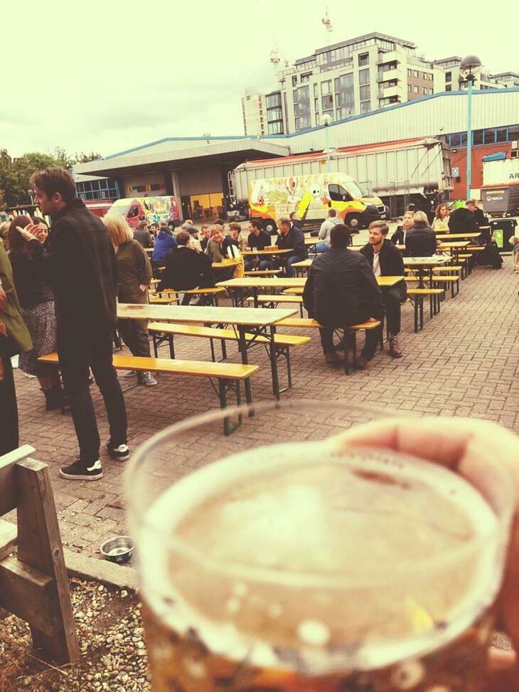 Brewery taprooms in London: A pint held in the foreground with people drinking on outside benches in the background