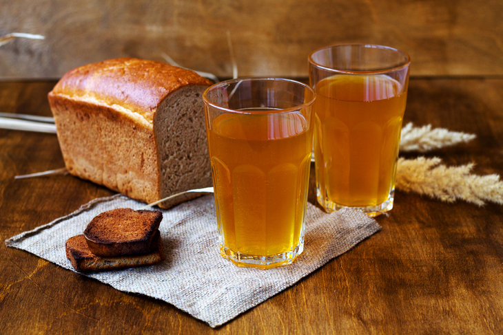 A loaf of bread next to two murky glasses of liquid which may or may not be ale