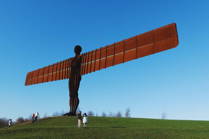 The angel of the north is captured in the centre of the image. It is a large metal structure that looks like a person holding their arms out to make a cross shape. The arms are like wings of an airplane. 