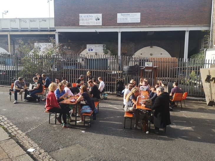 Brewery taprooms in London: People sitting outside on benches by railway arches, drinking in the sun