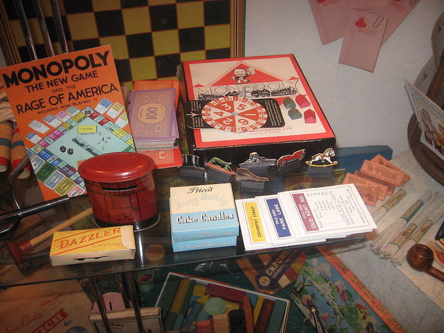 A glass table loaded with exhibits including an old Monopoly game, cake candles and a chess board