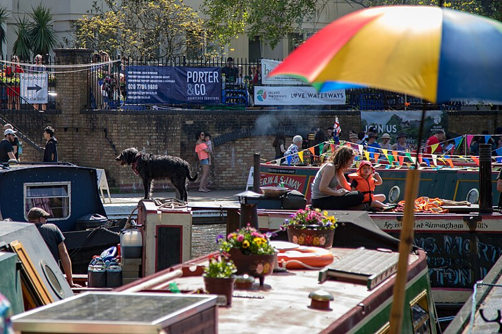Canalway Cavalcade: people sitting on boats moored up in Little Venice, with other people walking past on the towpath