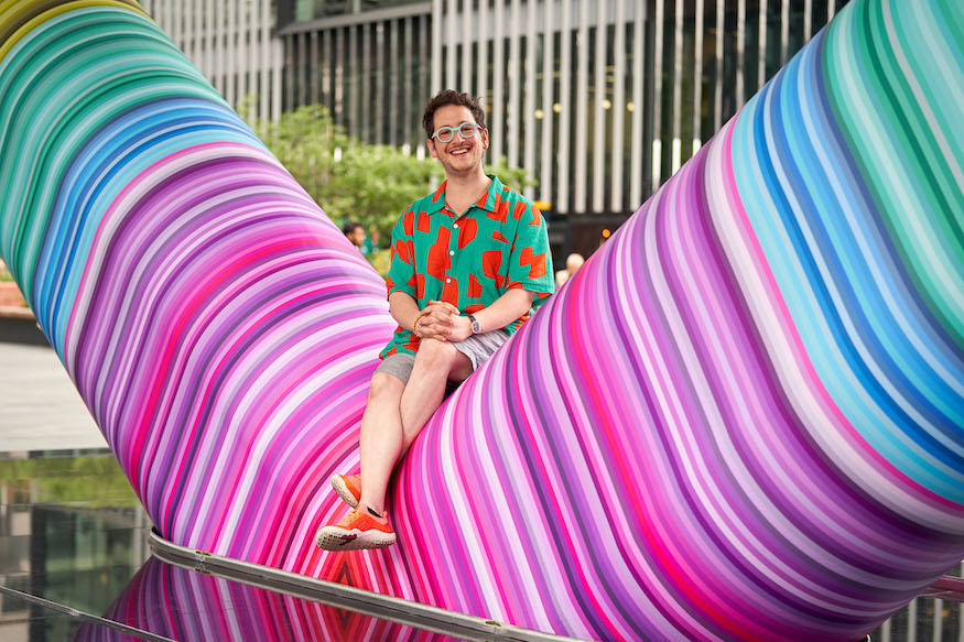 Artist Adam Nathaniel Furman sits on a colourful V-shaped support structure