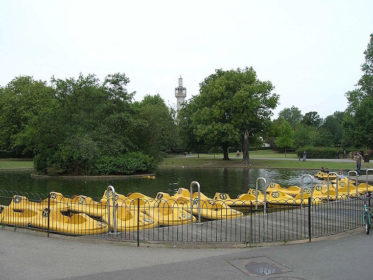 A group of yellow children's pedalos tied up at one side of a lake, with the Regent's Park Mosque in the background