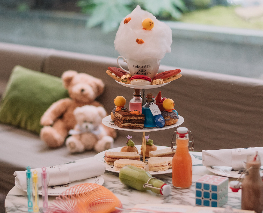 An Alice in Wonderland themed afternoon tea, with two teddy bears sitting on a seat in the background.