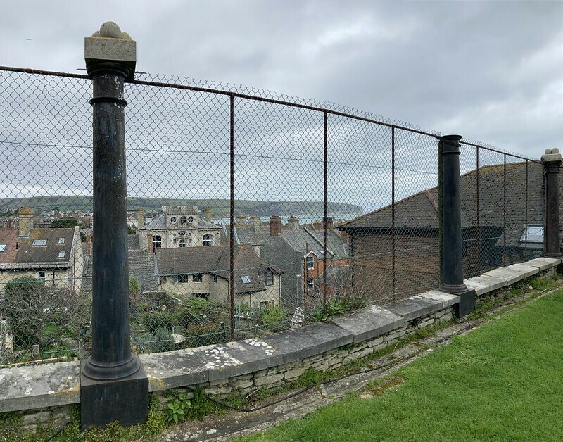 Sturdy black iron columns from billingsgate market holding up a wire fence with a view over Swanage