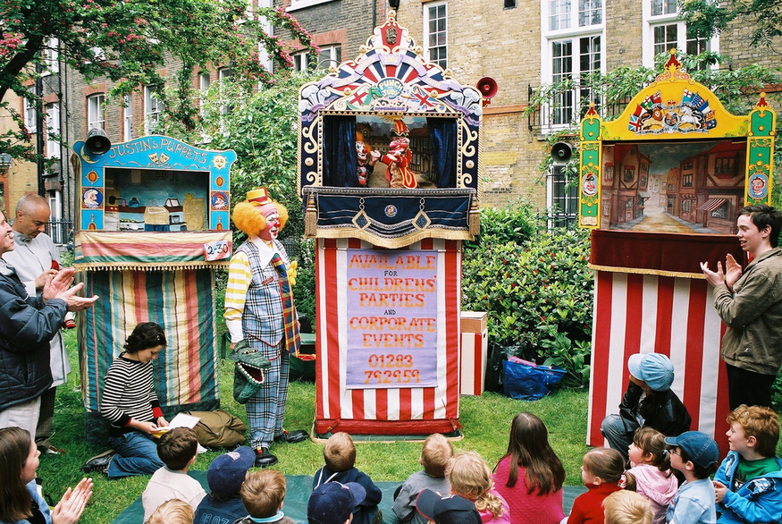 Children sitting on the grass watching a Punch & Judy show at the Covent Garden Puppet Festival