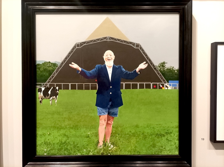 A portrait of a smiling Michael Eavis in front of the Pyramid Stage