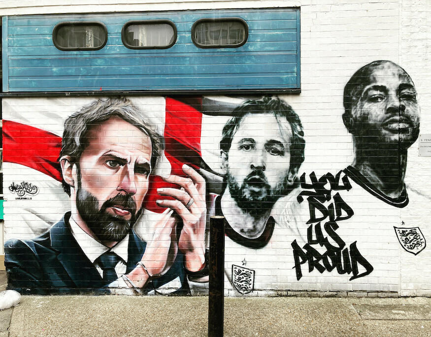 A mural showing Gareth Southgate applauding his players, two of whom are depicted in black and white against the England flag