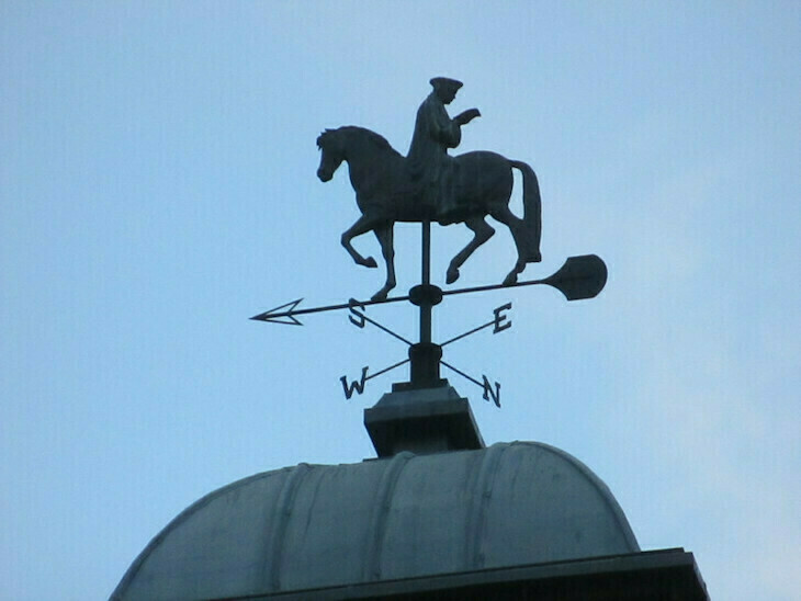 A weather vane of erasmus sat backwards on a horse reading a book above whitechapel gallery