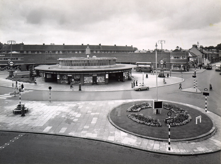 Black and white photo of the saucer-like station - with a roundel of flowers in the foreground
