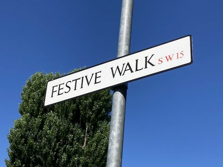 A london street sign on a post. It says festive walk sw15