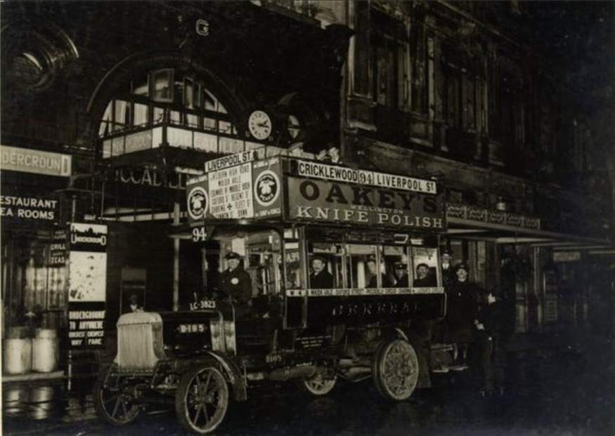 Black and white image of an old double decker bus plastered in adverts