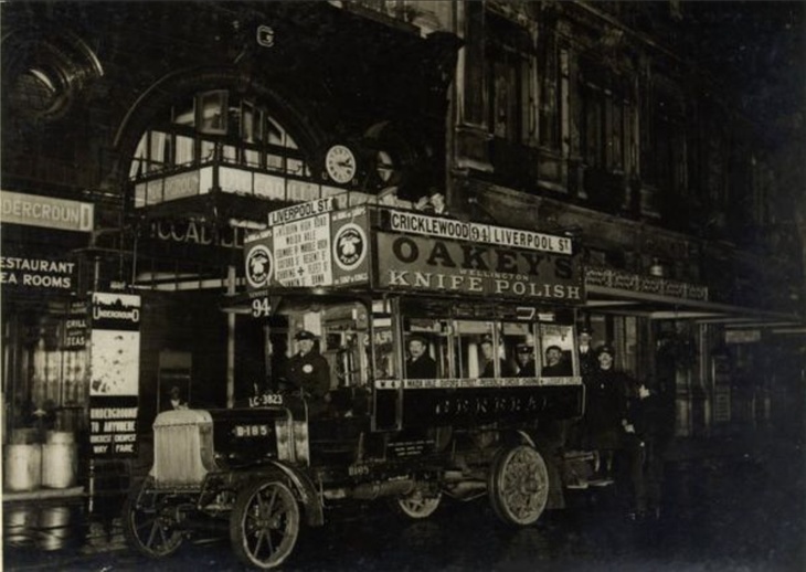 An old omnibus loaded with passengers outside a tube station
