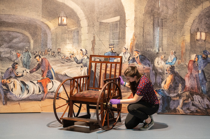 A lady in purple conservation gloves touches the wheel of florence nightingale's wheelchair