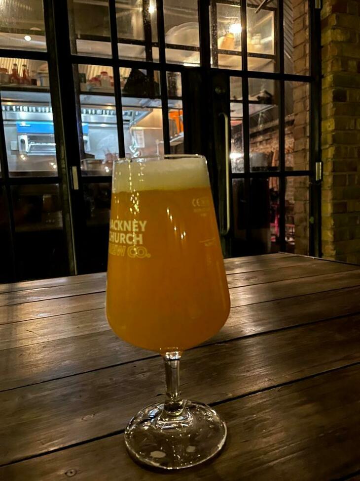 Brewery taprooms in London: A two-thirds glass of a dank looking beer on an outside table
