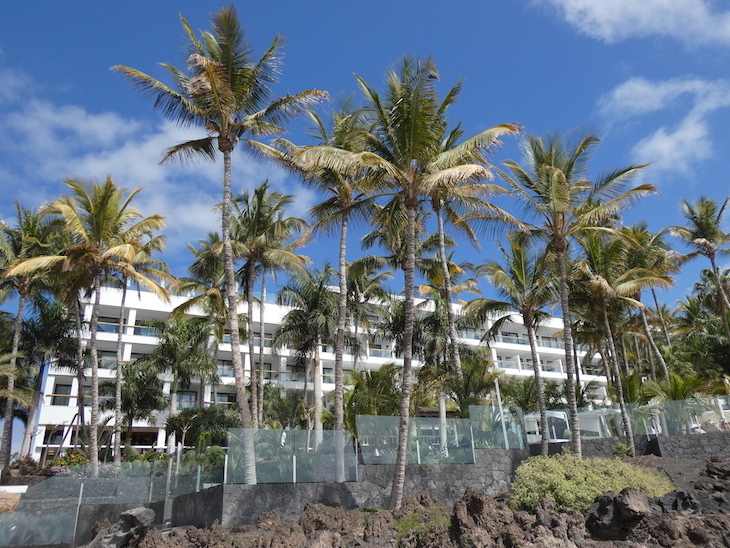 A hotel building up a cliff, with palm trees in its garden.