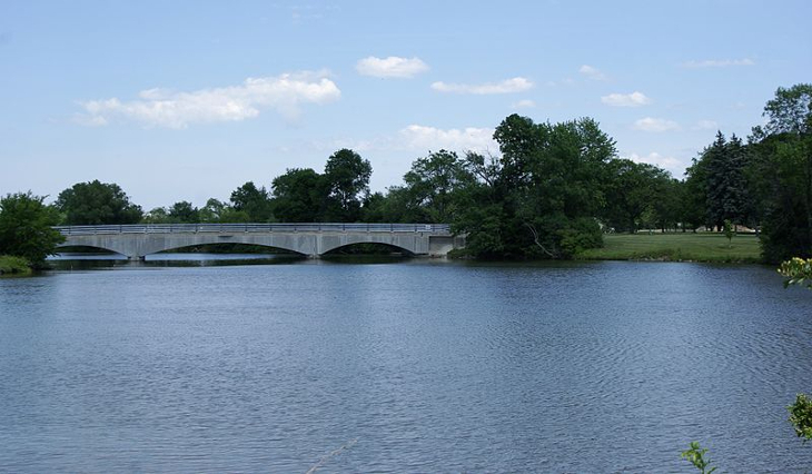 Looking across a lake towards a three-span concrete bridge, with trees on either side.