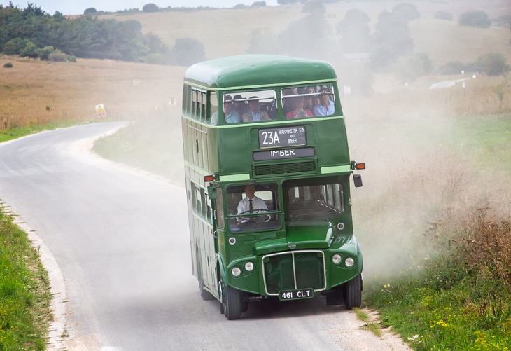 A green double decker Routemaster bus full of passengers on a road in the middle of nowhere, with no buildings or other vehicles around