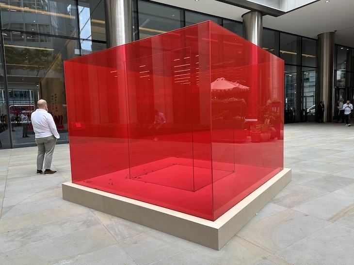 A red transparent cube in a city plaza