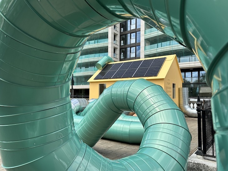Green pipes in a spiral with a yellow shed behind