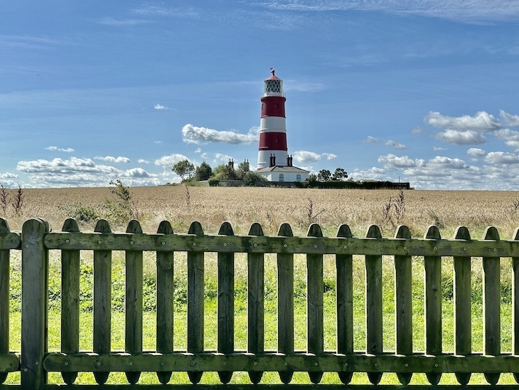 A red and white striped lighthouse in a field behind a picket fence