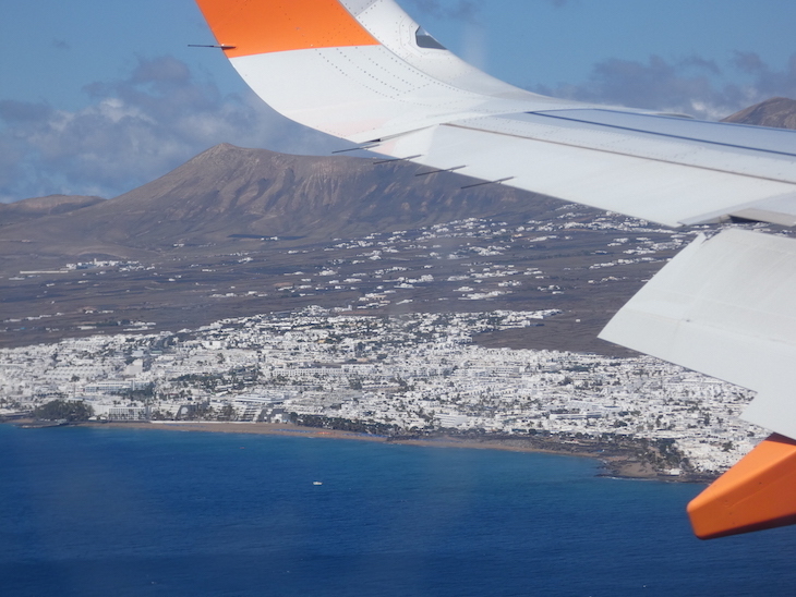 A photo taken from an aeroplane of the coastal town of Puerto del Carmen, with an aeroplane wing in the foreground.