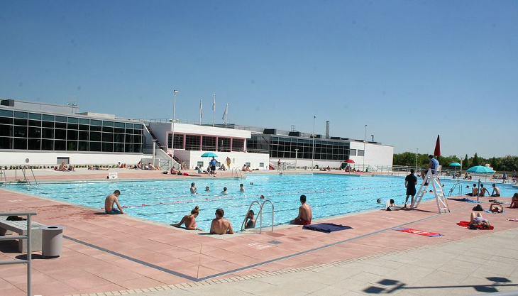 People swimming in and sunbathing alongside the outdoor pool at Hillingdon Lido in west London on a sunny day
