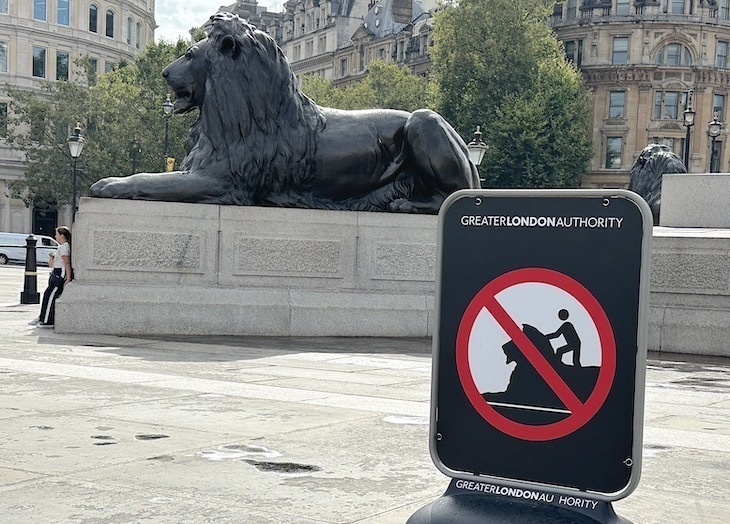 A Trafalgar Square lion with a sign in front of it saying not to climb on it