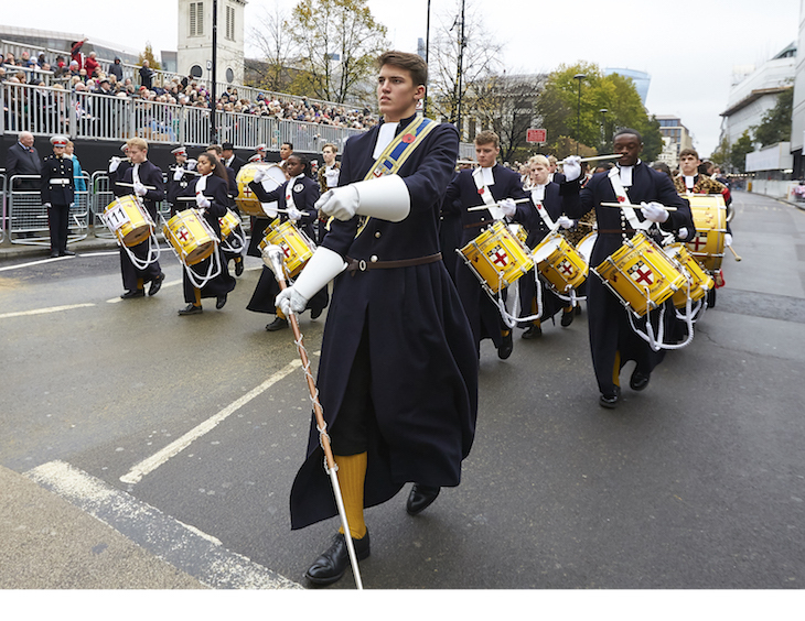 A military band dressed in long black robes and beating yellow drums, marches through the streets during the Lord Mayor's Show