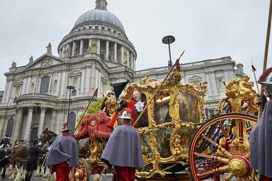 A former Lord Mayor leans out of the golden State Coach and waves at crowds, in front of St Paul's Cathedral
