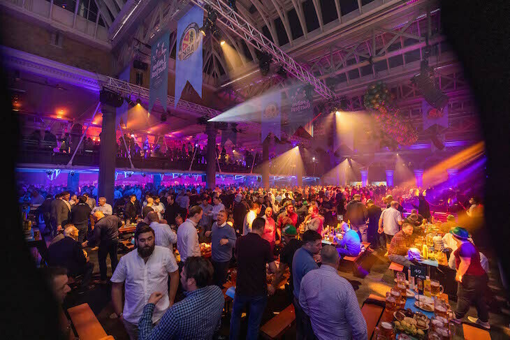London Oktoberfest  2023: Loads of people partying in a bier hall arena, with purple lighting