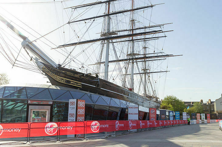 Greenwich's Cutty Sark, with 'Virgin Money' branded hoardings and railings set up outside to mark out the London Marathon route. Two marshalls in flourescent jackets can be seen in the distance but other than that , there are no runners or spectators