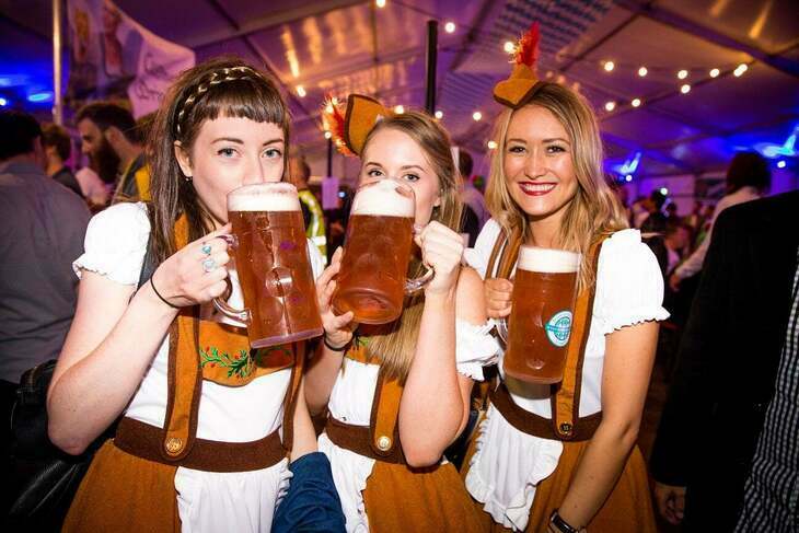 Three young women in traditional Bavarian clothing, holding steins of beer