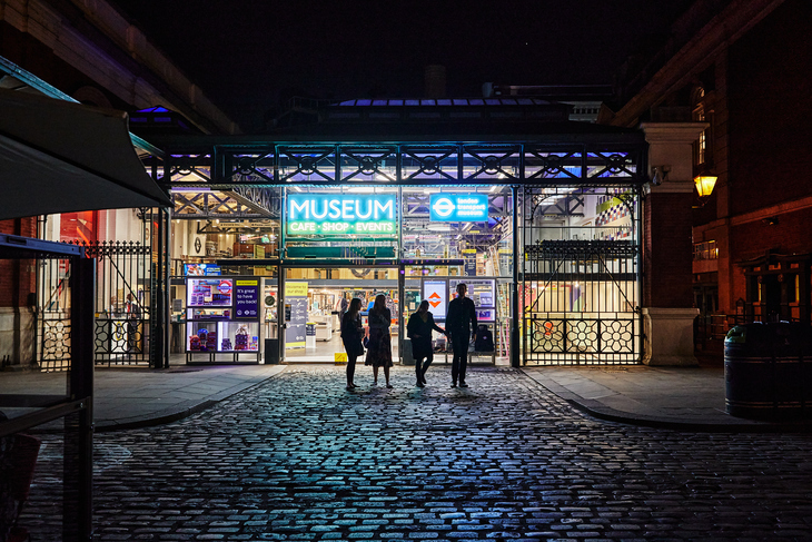 A group of people walking into the London Transport Museum at night - all lit up