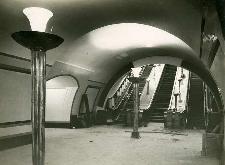 Black and white image of the bottom of the escalators with art deco lampposts