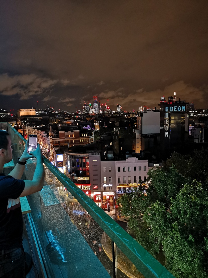 Best Rooftop Bars London: A man snaps a picture of Leicester Square at night from a balcony