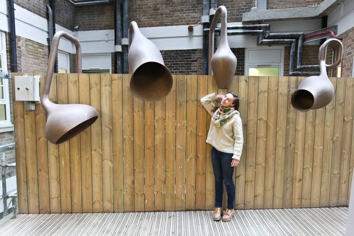 Free Things To Do In London: A woman puts her ear to numerous strange shaped listening horns which dangle over a fence