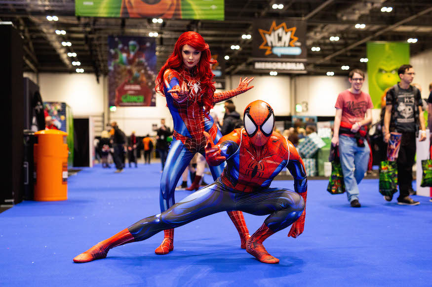 Someone dressed as Spiderman crouches on the ground, while a woman in Spiderman costume (without a mask) poses behind
