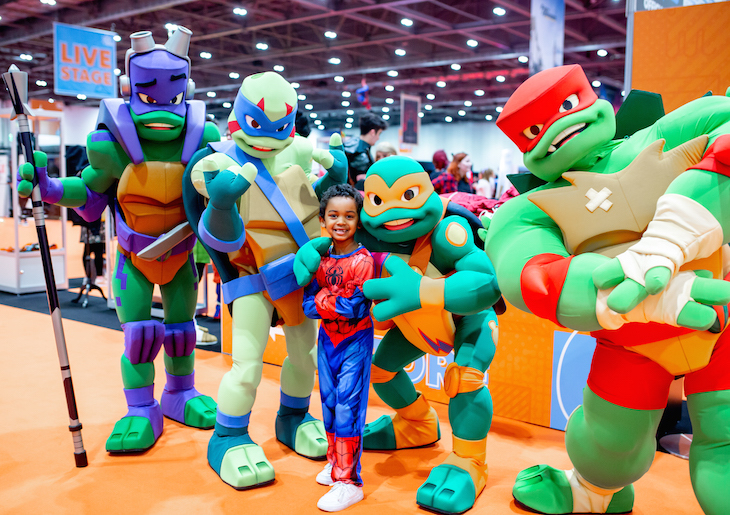 A child in a Spiderman costume poses with Ninja Warrior Turtle characters