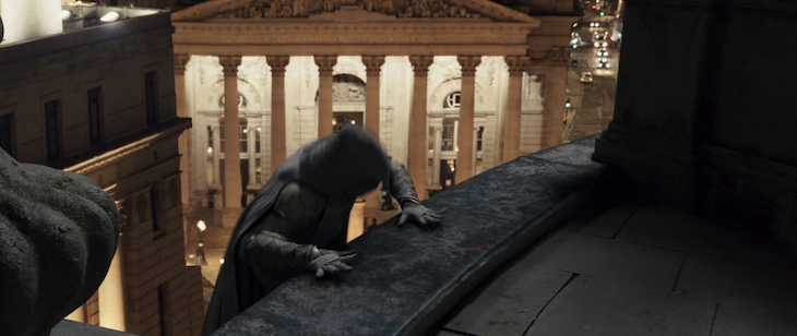 Moon Knight clambers on a roof in front of the Royal Exchange